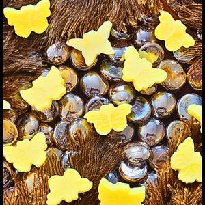 May include: A close-up shot features yellow butterfly-shaped objects scattered among brown feathers and iridescent glass beads. The butterflies have a smooth texture and are evenly spaced, creating a visually appealing arrangement. The beads reflect light, adding depth.