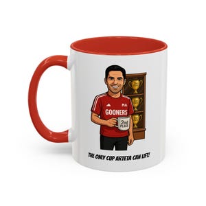 May include: A white ceramic mug with a red interior and handle. The mug features a cartoon illustration of a man in a red shirt holding a mug. The text on the mug reads "2nd Place". The mug also has the text "THE ONLY CUP ARTETA CAN LIFT!"