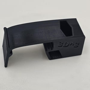 May include: A black 3D-printed component with the text "3D43" on the side. The object features a curved top and a rectangular base with cut-out sections. It is likely a small, functional part, possibly for a larger device or system.