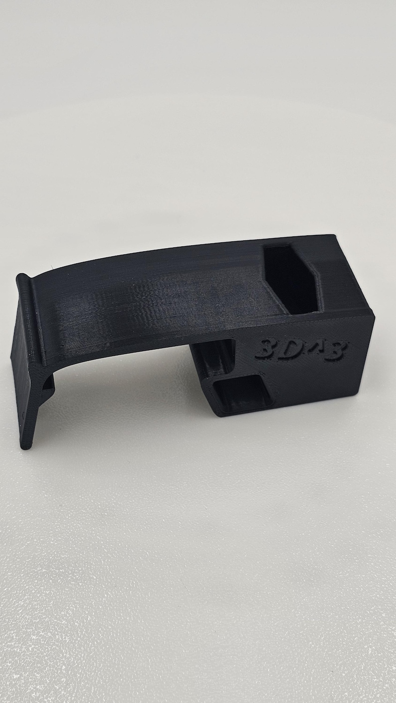 May include: A black 3D-printed component with the text "3D43" on the side. The object features a curved top and a rectangular base with cut-out sections. It is likely a small, functional part, possibly for a larger device or system.