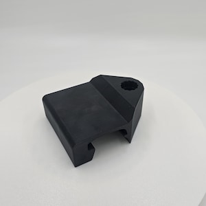 May include: A solid black plastic component with a geometric design. It features a rectangular base with a curved edge and a raised section with a circular hole. The object is likely a part of a larger mechanism or structure.