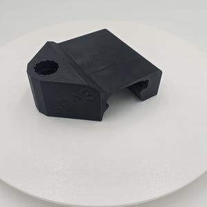 May include: A black, angular object with a textured surface. The object has a hexagonal hole and the number "3D A3" is visible on the side. The item is likely a 3D-printed component or part.