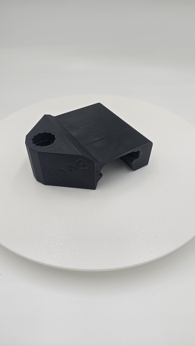 May include: A black, angular object with a textured surface. The object has a hexagonal hole and the number "3D A3" is visible on the side. The item is likely a 3D-printed component or part.