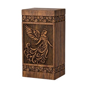 Op de afbeelding: Houten urn met een donkerbruine afwerking. Het voorpaneel heeft een gedetailleerde gravure van een engel met uitgespreide vleugels. De boven- en onderranden zijn versierd met een blad- en wijnrankenontwerp. Een waardig gedenkteken.