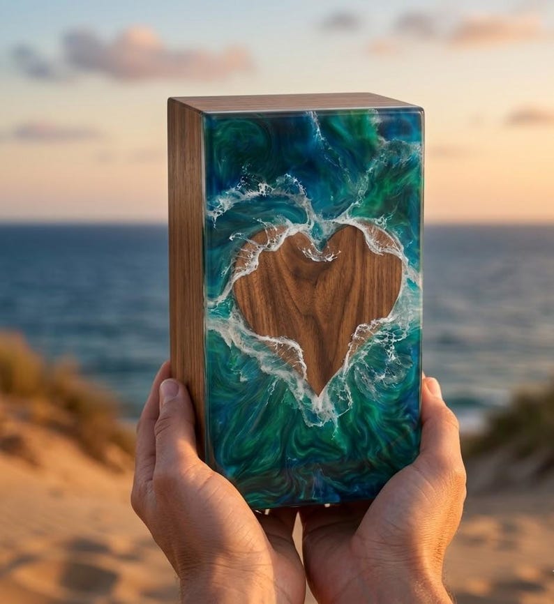 May include: A wooden box with a heart-shaped cutout, filled with blue and green resin that resembles ocean waves. The box is held up against a beach and ocean background.
