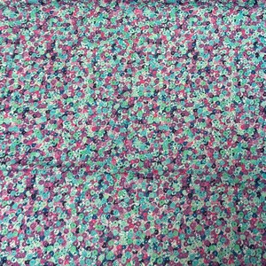 May include: A fabric with a dense floral pattern. The design features small, closely packed flowers in shades of pink, purple, blue, and green on a white background. The overall effect is a colorful, textured surface.