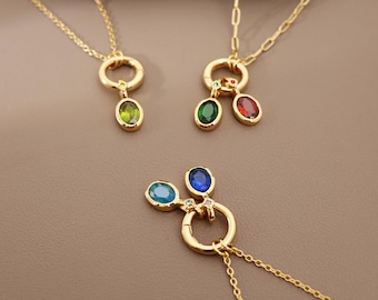May include: Gold-toned necklaces with colorful gemstone pendants. Each necklace features a delicate chain and a circular pendant holding oval-shaped gemstones in various colors, including green, red, blue, and teal.