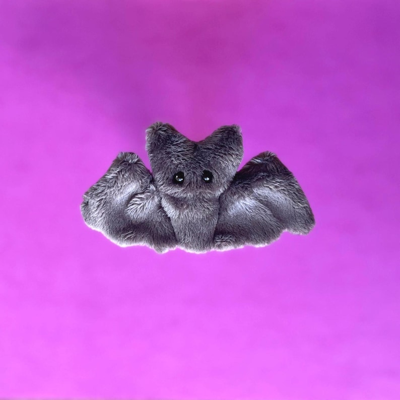 Pu&ograve; includere: Un giocattolo di peluche grigio a forma di pipistrello, con grandi occhi e ali spiegate. Il pipistrello &egrave; fatto di materiale morbido e sfocato su uno sfondo viola brillante. Ideale per Halloween o come compagno coccoloso. Circa 20 cm di larghezza.