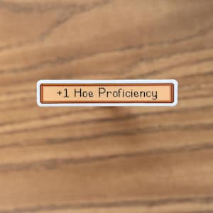May include: A rectangular sticker with a white border and a tan center. The text "+1 Hoe Proficiency" is displayed in black pixelated font. The sticker is set against a wooden background.
