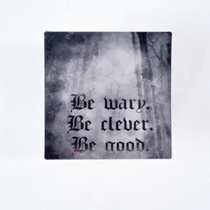 May include: Square decorative item with a forest scene background and the words "Be wary. Be clever. Be good." in gothic script. The text is in black, with a touch of red on the word "good".