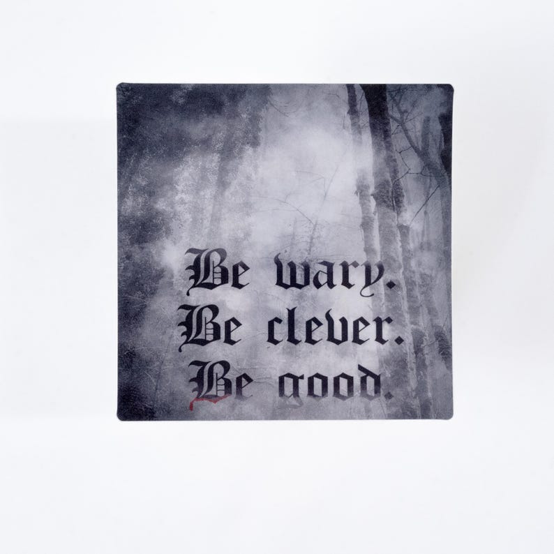 May include: Square decorative item with a forest scene background and the words "Be wary. Be clever. Be good." in gothic script. The text is in black, with a touch of red on the word "good".