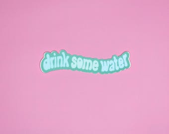 May include: A sticker with the text "drink some water" in a light blue, wavy font, outlined in white. The sticker is set against a solid pink background.