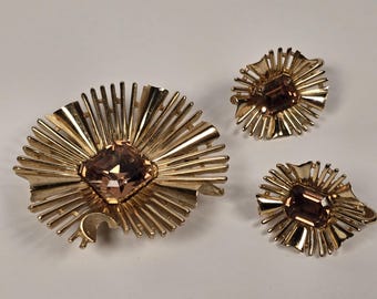 Peut inclure: Un ensemble de bijoux vintage comprenant une broche et des boucles d'oreilles assorties. La broche et les boucles d'oreilles présentent un motif en forme d'éclat de soleil avec une pierre précieuse centrale, taillée en carré, de couleur marron clair.