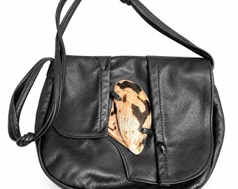May include: A black leather shoulder bag with a textured surface, featuring a long adjustable strap with knotted ends and a large, irregular, cream and dark brown patterned shell-like decorative accent secured on the front flap.
