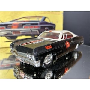Puede incluir: Un coche de juguete de metal negro con techo blanco, que presenta una franja de carreras roja en el capó y el texto rojo Holman Moody en el lateral. El vehículo tiene ruedas plateadas, un parachoques delantero cromado y un interior rojo visible.