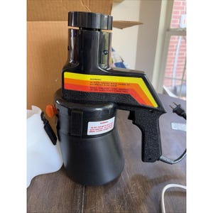 May include: Black and yellow paint sprayer with a handle and attached container. The sprayer has a black body with a yellow, orange, and red stripe design. The container is white and has an orange handle. The sprayer has a warning label.