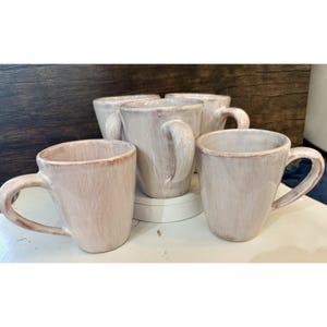 May include: Five ceramic mugs in a neutral colour palette. The mugs have a rustic, handmade appearance with visible brushstrokes and a slightly textured surface. Each mug features a curved handle and a wide opening.