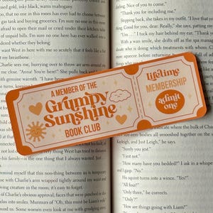 May include: An orange bookmark with the text "A MEMBER OF THE Grumpy Sunshine BOOK CLUB" and "Lifetime MEMBERSHIP admit one" over an open book. The bookmark has a sun, cloud, and heart design.