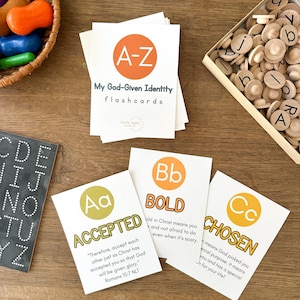 Può includere: Flashcard bianche con il testo "My God-Given Identity flashcards" e le lettere A-Z. Le carte presentano le parole "Accepted", "Bold" e "Chosen". Sono visibili anche lettere di legno e giocattoli colorati.