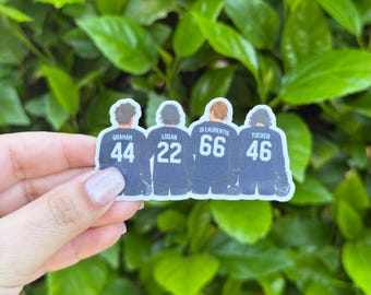 Puede incluir: Una pegatina con cuatro figuras con camisetas azul marino con números y nombres blancos: Graham (44), Logan (22), Di Laurentis (66) y Tucker (46). La pegatina está sobre un fondo de follaje verde.