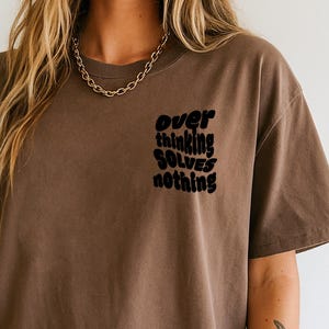May include: Espresso-colored t-shirt with the text "over thinking solves nothing" in black. The shirt has a relaxed fit and is labeled "high quality embroidery" and "Espresso Comfort Colors".