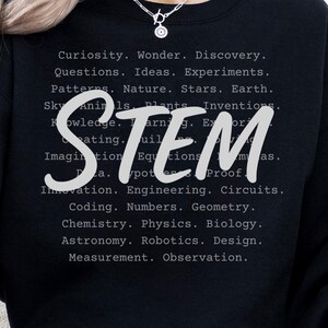 以下が含まれることがあります： 黒いSTEMスウェットシャツ。STEM関連の単語が薄いグレーのフォントでリストされています。「STEM」という単語は、様式化された白いフォントで書かれています。「BLACK」という単語は、黒い楕円の中に白いフォントで書かれています。