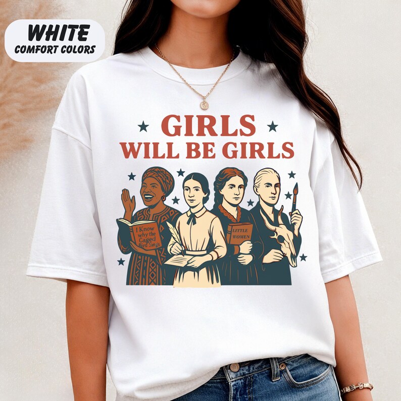 May include: White t-shirt with the text "GIRLS WILL BE GIRLS" in red and a graphic of four women. The shirt also has the text "WHITE COMFORT COLORS" in the upper left corner. The women are holding books, pens, and a paintbrush.