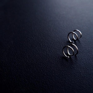 May include: A close-up of three silver metal spring coils on a black surface.