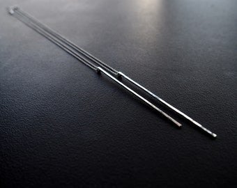 May include: A silver necklace with two long, thin, rectangular pendants hanging from it. The necklace is on a black surface.