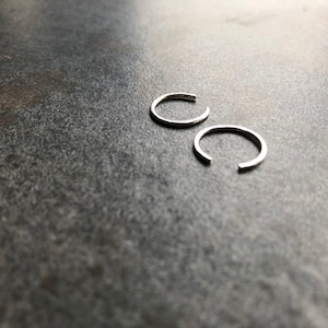 May include: Two silver ear cuffs, a popular jewelry style, are shown on a gray textured surface.