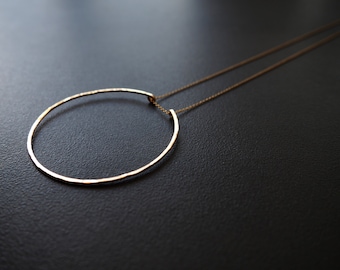 May include: A gold necklace with a hammered circle pendant. The necklace is on a black background.