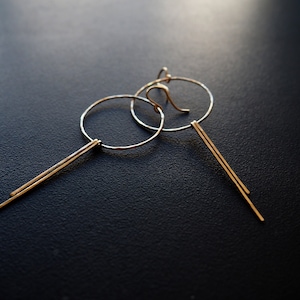 May include: A pair of gold hoop earrings with a long, thin, straight bar hanging from each hoop.