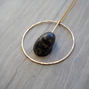 May include: A gold necklace with a hammered circle pendant and a black stone hanging from the bottom.