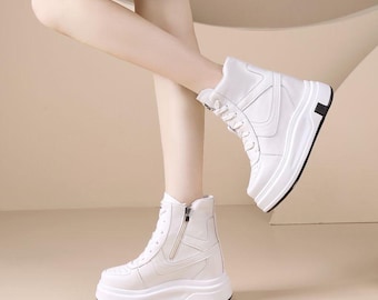Puede incluir: Zapatillas altas blancas con suela gruesa. Las zapatillas tienen cierre de cordones y cremallera lateral. El diseño incluye detalles cosidos y un acento negro en el talón. Los zapatos están hechos de un material liso similar al cuero.