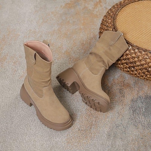 Könnte beinhalten: Ein Paar hellbraune Wildlederstiefel mit klobiger Profilsohle. Die Stiefel haben eine mittlere Wadenhöhe und eine runde Spitze. Die Innenseite ist hellrosa. Die Stiefel stehen vor einem neutralen Hintergrund.
