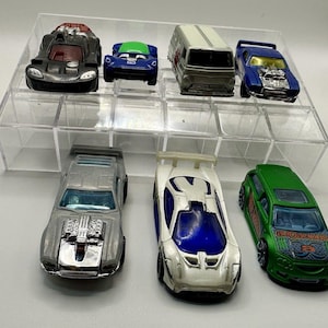 May include: A collection of toy cars in various colors, including black, blue, silver, white, and green. The cars are displayed on a clear plastic organizer. Some cars have detailed engine components.