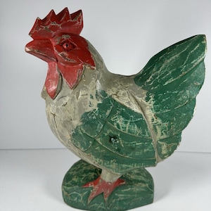 May include: A hand-carved wooden rooster figurine. The rooster features a red comb and wattle, green wings, and red feet. The body is painted in shades of gray and green, with a distressed finish. The figurine is a decorative item.