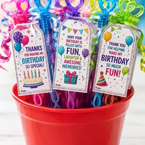 May include: A red bucket filled with bubble wands, each topped with a heart-shaped or crown-shaped handle. The wands have tags with birthday messages and colorful graphics, including balloons and a birthday cake.