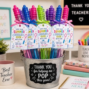 Może przedstawiać: Ocynkowane metalowe wiadro wypełnione kolorowymi patyczkami do baniek mydlanych, każdy ozdobiony etykietą z napisem "Hope Your Summer Bubbles Over With Fun!" i różową wstążką. Kubek mówi "Best Teacher Ever".
