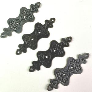 May include: Four antique-style metal decorative corner brackets. Each bracket is dark gray with a floral design and two small holes for mounting. The brackets have a curved shape with decorative ends.