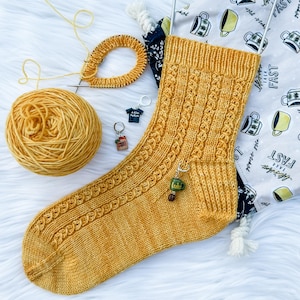 Peut inclure: Une chaussette tricotée à la main jaune moutarde avec un motif torsadé, accompagnée d'une pelote de laine assortie, d'aiguilles à tricoter circulaires et de trois petits charms en forme de t-shirt, de sac de courses et de tasse verte marquée Luke.
