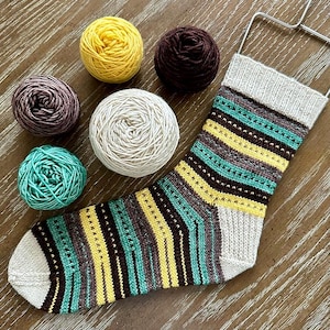 May include: A hand-knitted sock with a striped pattern in yellow, teal, brown, and gray, alongside several balls of yarn in coordinating colors. The sock is displayed on a metal sock form, showcasing the intricate stitch work and color palette.