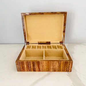 May include: Open wooden jewelry box with a light tan interior and multiple compartments. The box is rectangular with a hinged lid and is made of wood with a striped pattern.