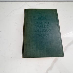 Puede incluir: Un libro antiguo de tapa dura con una cubierta verde oscuro. El t&iacute;tulo "RALPH WALDO EMERSON" est&aacute; grabado en letras doradas. El libro tiene un aspecto texturizado y est&aacute; ligeramente desgastado, lo que sugiere antig&uuml;edad.