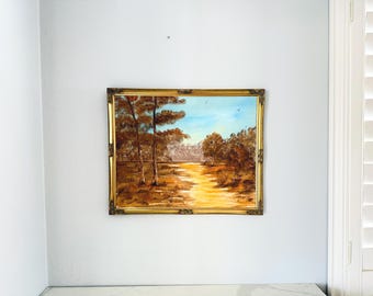 Op de afbeelding: Een landschapsolieverfschilderij in een versierde goudkleurige lijst met een zonnig zandpad dat door een bos van bruine en oranje bomen slingert onder een lichtblauwe lucht, met twee kleine vogels die in de verte vliegen in een herfsttafereel.