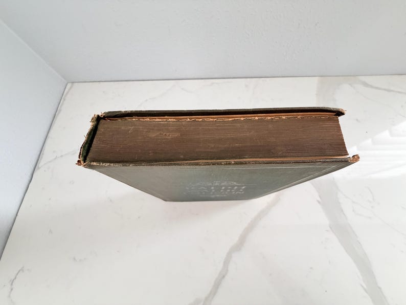 Puede incluir: Un libro antiguo con una cubierta verde oscuro y p&aacute;ginas envejecidas con tonos marrones. El lomo y los bordes del libro muestran signos de desgaste, lo que sugiere su edad. El t&iacute;tulo es visible en la portada. El libro est&aacute; sobre una superficie blanca.
