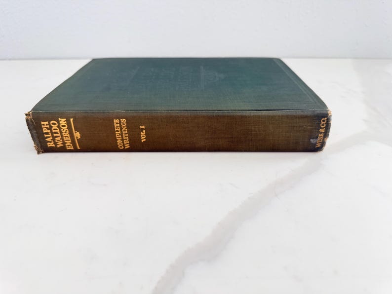 Puede incluir: Un libro antiguo titulado "Complete Writings Vol. I" de Ralph Waldo Emerson. El libro tiene una cubierta verde oscuro y un lomo marr&oacute;n con letras doradas. El libro es de Wise & Co.