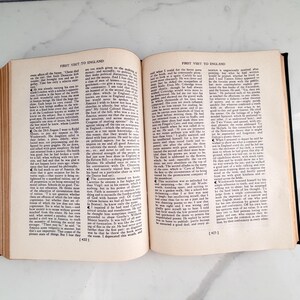 Puede incluir: Un libro abierto con el t&iacute;tulo "FIRST VISIT TO ENGLAND" impreso en la parte superior de cada p&aacute;gina. Las p&aacute;ginas est&aacute;n llenas de texto negro peque&ntilde;o. El libro tiene una cubierta negra y est&aacute; sobre un fondo blanco.