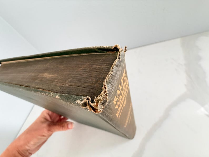 Puede incluir: Un libro antiguo con una cubierta verde oscuro y letras doradas. Los bordes del libro muestran desgaste, con las esquinas y el lomo mostrando signos de edad. El t&iacute;tulo "RALPH WALDO EMERSON" es visible en la portada.