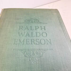 Puede incluir: Un libro antiguo con una cubierta verde descolorida. El t&iacute;tulo "RALPH WALDO EMERSON" est&aacute; grabado en letras may&uacute;sculas grandes. Adornos decorativos se encuentran arriba y abajo del t&iacute;tulo, agregando un toque cl&aacute;sico.